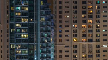 Çok öykülü modern cam konut içinde parlayan pencere eşiği ışık gece timelapse bina. Daireler insanlar. Akşam aydınlatılmış gökdelenler. Dubai Yat Limanı ve Jbr, Birleşik Arap Emirlikleri.