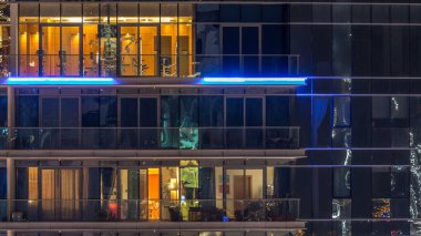 Çok öykülü modern cam ve metal kadar ışık gece timelapse bina konut içinde parlayan pencere eşiği. Daireler insanlar. Geceleri aydınlatılan evler. Dubai, Birleşik Arap Emirlikleri. Aşağı kaydır