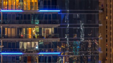 Çok öykülü modern cam ve metal kadar ışık gece timelapse bina konut içinde parlayan pencere eşiği. Daireler insanlar. Geceleri aydınlatılan evler. Dubai, Birleşik Arap Emirlikleri. Yakınlaştır