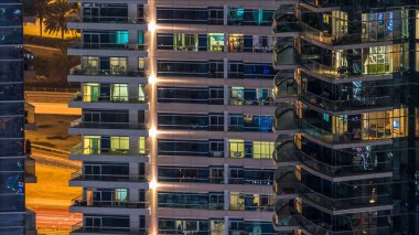 Çok öykülü modern cam ve metal kadar ışık gece timelapse bina konut içinde parlayan pencere eşiği. Daireler insanlar. Geceleri aydınlatılan evler. Dubai, Birleşik Arap Emirlikleri. Pan sol