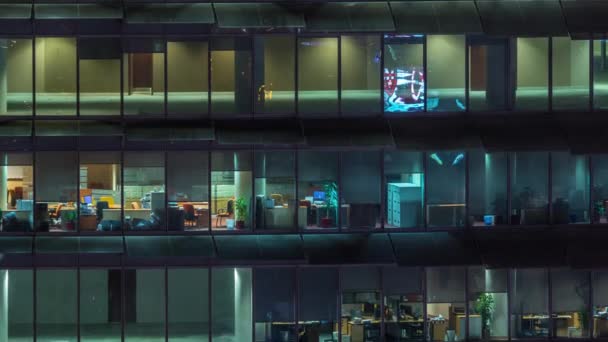 ガラスの壁と窓のタイムラプスを持つ多数のオフィスを持つガラスオフィスビルで働く夕方 — ストック動画