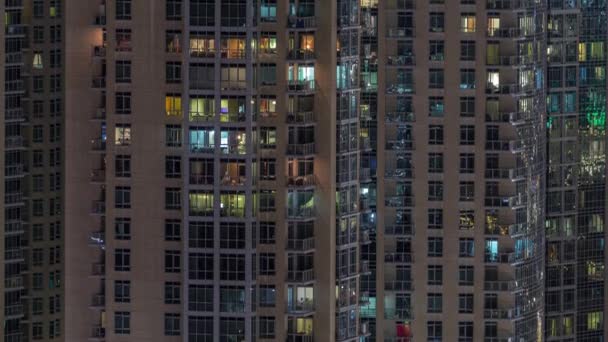 Παράθυρα του πολυορόφου κτιρίου με φωτισμό μέσα και μετακινώντας τους ανθρώπους σε διαμερίσματα. — Αρχείο Βίντεο