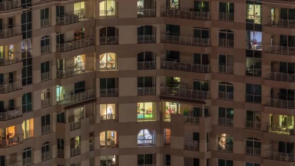 Ventanas del edificio de varios pisos con iluminación interior y personas en movimiento en apartamentos timelapse . — Vídeo de stock