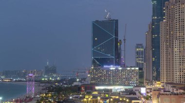 Dubai, Bae'de gece saatlerinden geceye gökdelenlerle Jbr'de yürüyen plaj ve turistlerin havadan görünümü