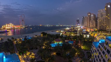 Dubai, Bae'de gece saatlerinden geceye gökdelenlerle Jbr'de yürüyen plaj ve turistlerin havadan görünümü