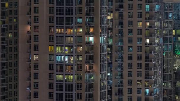 Παράθυρα του πολυορόφου κτιρίου με φωτισμό μέσα και μετακινώντας τους ανθρώπους σε διαμερίσματα. — Αρχείο Βίντεο