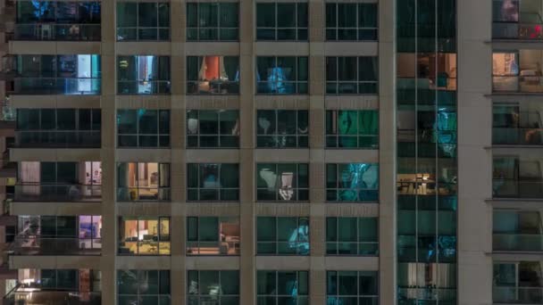 Okna vícepodlažní budovy s osvětlením uvnitř a přesunem osob v apartmánech. — Stock video