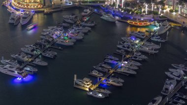 Dubai marina gece zaman atlamalı yüzen yatlar havadan görünümü. Beyaz tekneler kanal suyunda.