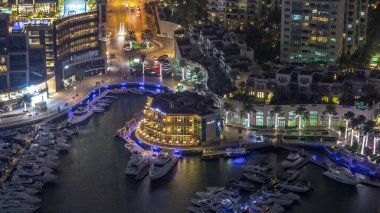 Dubai marina gece zaman atlamalı yüzen yatlar havadan görünümü. Beyaz tekneler kanal suyunda.