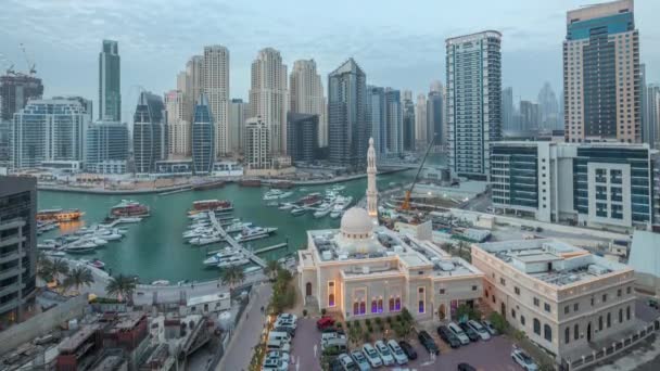 Jachten in Dubai Marina geflankeerd door de Al Rahim moskee en residentiële torens en wolkenkrabbers antenne dag tot nacht timelapse. — Stockvideo