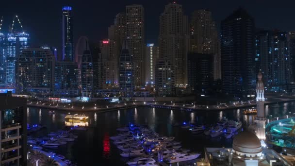 Jachten in Dubai Marina geflankeerd door de Al Rahim moskee en residentiële torens en wolkenkrabbers antenne nachtzicht — Stockvideo