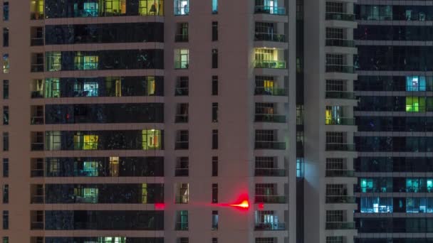 Barisan jendela bercahaya dengan orang-orang di gedung apartemen di malam hari . — Stok Video
