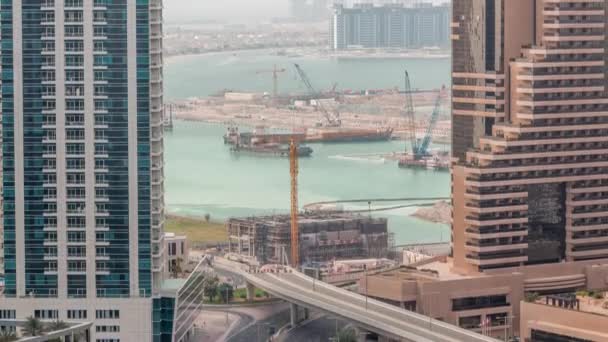 Vista aérea de los rascacielos del puerto deportivo de Dubái con obras de construcción y Palm Jumeirah Island en el timelapse de fondo . — Vídeos de Stock