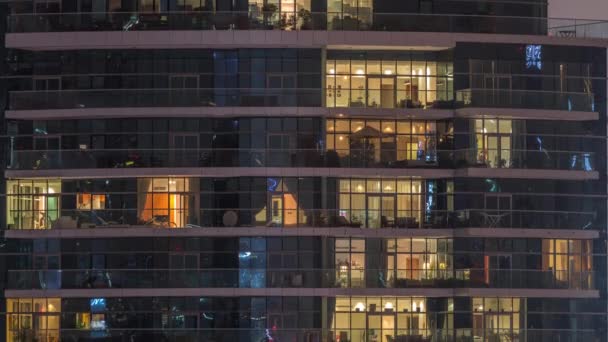 Filas de ventanas brillantes con gente en el edificio de apartamentos por la noche . — Vídeo de stock