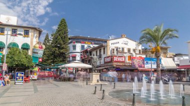 Antalya 'daki Cumhuriyet Meydanı' nda çok sayıda kafe ve bar, Attalos II 'nin heykeli ve hediyelik eşya dükkanları bulunuyor. Çeşme ön planda. Yazın mavi bulutlu gökyüzü
