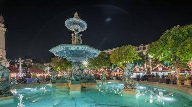 Portekiz, Lizbon 'un Baixa bölgesindeki Dom Pedro IV Meydanı' ndaki Rossio Noel Pazarı 'nda akşam süslemeleri ve yemek kabinleriyle aydınlatılmış çeşmeyi gösteren panorama..