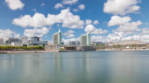 Panorama showing Parque das Nacoes or Park of Nations district timelapse in Lisbon, Portugal. Telecabine cable cars overlook Vasco da Gama bridge on Tagus river. Modern buildings reflected in water