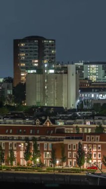 Geceleri Katendrecht yarımadasının panoramik zaman çizelgesi ve Hollanda Rotterdam 'daki Maashaven limanı. Aydınlatılmış şehir silüeti ve modern kuleleri olan geleneksel Hollanda rıhtım evleri