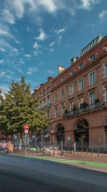Toulouse, Occitanie, Fransa 'da Rue de Metz' in zaman çizelgesini gösteren panorama, tarihi cepheleri, dükkanları, kafeleri, trafiği ve mavi bulutlu gökyüzünü gösteriyor. Şehrin göbeğinde canlı bir şehir manzarası