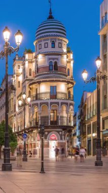 Avenida de la Constitucion, Seville, İspanya 'da günden geceye zaman dilimi. Iconic Adriatica binası gün batımından sonra parlıyor. Modern sokak lambaları, yayalar ve şehir atmosferine sahip tarihi mimari
