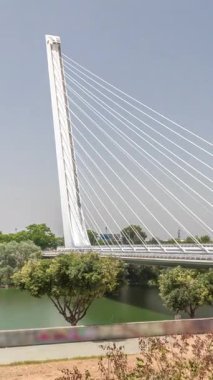 İspanya 'nın Sevilla kentindeki Guadalquivir Nehri' nin üzerinden geçen uzun kolon ve çelik kablolu Alamillo Köprüsü. Açık mavi gökyüzü altında yoğun trafik ile modern süspansiyon tasarımının hızlandırılmış zamanlaması.