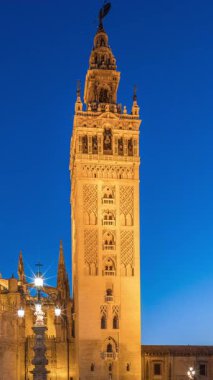 La Giralda ve Seville Katedrali günden geceye geçiş zamanı, gün batımından sonra altın ışıklarla parıldıyor. Tarihi çan kulesi, gotik detaylar ve Seville, İspanya 'da aydınlatılmış sokaklar.