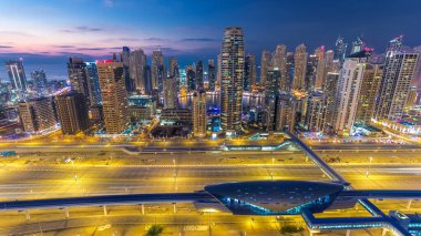 Dubai Marina ve Dubai, BAE 'deki JLT gökdelenlerinin hava üzerinden gece gündüz geçiş zamanı. Modern kuleler ve Şeyh zayed yolundaki trafik yukarıdan metro ve tramvay istasyonlarıyla