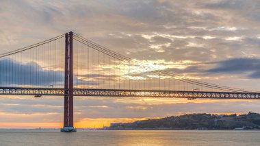 Lisbon city sunrise with April 25 bridge timelapse, River and waterfront early morning. Orange clouds on the sky
