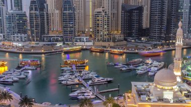 Dubai Marina 'daki yatlar El Rahim Camii' nin, yerleşim kulelerinin ve gökdelenlerin, hava gününden geceye geçiş zamanlaması ile çevrili. Tekneler ve ahşap çayırlarla modern gökdelenler.