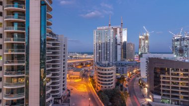 Dubai Marina 'da aydınlık gökdelenler ve gece gündüz gezinti güvertesi geçiş zamanı. Yol trafiği olan modern kuleler ve tekneler. Birleşik Arap Emirlikleri