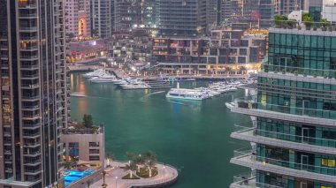 Dubai Marina yerleşim yerlerinin ve ofis gökdelenlerinin havadan görüntüsü. Rıhtımdan geceye geçiş zamanı. Yüzen tekneler ve yatlar