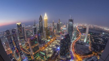 Sheikh Zayed Yolu yakınlarındaki binaların silueti ve Dubai, BAE 'deki hava gününden geceye geçiş. Günbatımından sonra finans merkezinde ve şehir merkezinde park yeri olan modern kuleler ve gökdelenler.