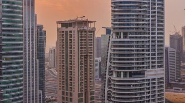 Dubai'de Jumeirah göl kuleleri ilçe timelapse konut ve ofis binaları üzerinde gün batımı. Modern gökdelenler ile yukarıdan havadan panoramik görünüm