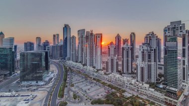 Günbatımında Business Bay, Dubai, Uae 'de bulunan birçok gökdelenle modern yerleşim ve ofis kompleksi. Körfez Bulvarı Parkı 'nın yanındaki büyük otoparkta arabalar ve trafik vardı.