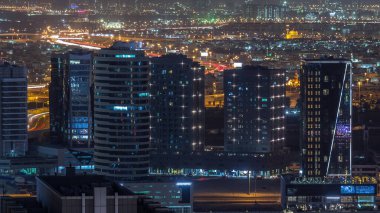 İş sahasında gece gündüz kuleler aydınlandı. Gece geçiş zamanı. Bazı gökdelenlerin çatı manzarası ve inşaat halindeki yeni kuleler. Otoyolda trafik ve pencerelerde ışıklar