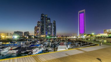 Al Bateen marinası Abu Dabi. Gün batımından sonra tekneler ve arka planda aydınlatmalı modern gökdelenler.