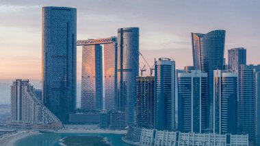 Abu Dabi 'deki Al Reem' deki gökdelenler gün doğumunda gökdelenler. Al Reem Adası 'ndan sabah sisli bir şehir manzarası. Güneş cam yüzeyine yansıyor