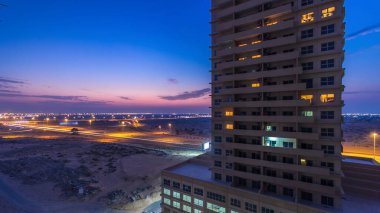 Ajman 'da çatıdan gece kuleye kule ve kavşakta trafik olan şehir manzarası. Birleşik Arap Emirlikleri 'nde gün batımından sonra aydınlanan binaların hava manzarası.