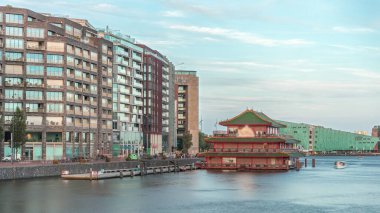 Sudaki pagoda şeklinde bir Çin restoranının hipervanesi, tarihi şehir merkezi binalarının ve günbatımında modern mimarinin arka planına karşı kurulur. Amsterdam, Hollanda