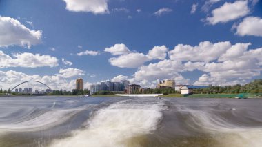 Astana, Kazakistan. Keyif teknesinden Astana 'da Ishim nehrinde hareketli bir seyahat görüntüsü. Mavi gökyüzü ve bulutlarla dolu bir yaz gününde. Bulanık hareket