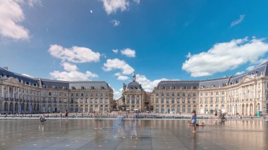 Place de la Bourse ve Miroir d 'eau hiperlapse Bordeaux, Fransa' da, tarihi mimariyi yansıtıyor. Turistler şehir simgesi ve çeşmenin tadını çıkarıyorlar. Trafik ve tramvay zamanı geçiyor..