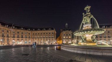 Panorama, Place de la Bourse 'u ve Fransa' nın Bordeaux şehrindeki çeşmeleri gösteriyor. Aydınlatılmış tarihi binalar büyük meydanın sınırında. Trafik ve sokakta hareket sahneyi güçlendirir