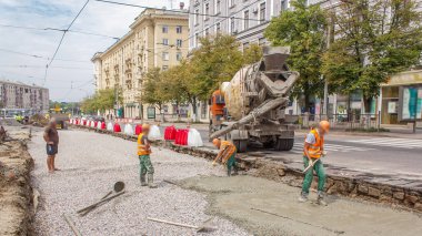 Turuncu üniformalı ve mikser makineli işçilerle yol inşaatı için beton döşeme ve seviyelendirme. Tramvay raylarının yeniden inşası
