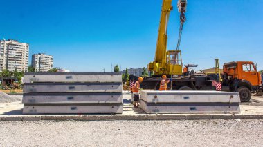Yol inşaatı zamanında sarı vinçle beton plakaları boşaltıyorum. Şapkalı ve üniformalı endüstriyel işçiler. Şehir caddesindeki tramvay raylarının yeniden inşası