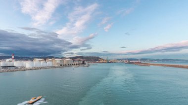 Gün batımında açık denizde yelken açan gemiden dalgalı ve limanlı deniz manzarası. Barselona kıyısı, İspanya