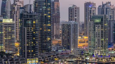 Lüks Dubai Marina Kanalı 'ndan geçen tekneler ve gece gündüz restoranlarla gezinti günbatımından sonra aydınlık gökdelenlerle yukarıdan manzaralı. Dubai, Birleşik Arap Emirlikleri