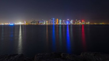 Doha şehir merkezi ufuk çizgisi günden geceye geçiş zamanı, Katar, Orta Doğu. Batı Körfezi 'ndeki aydınlık gökdelenler Körfez suyuna yansıyor.