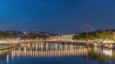 Lyon 'daki Saone Nehri' nin üzerindeki Palais du Justice Köprüsü 'nde, günden geceye geçiş. Rıhtımdaki aydınlık binalar gün batımından sonra suya yansıyor.