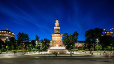 Sforza Kalesi 'nin ana girişi, ön manzara ve kule Castello Sforzesco, geçiş zamanı olan Milan, İtalya' yı aydınlattı. Çeşme ve etrafta dolaşan insanlar.