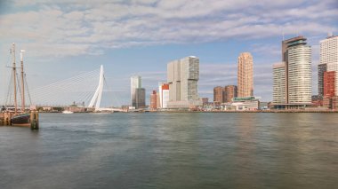 Panorama, Nieuwe Maas River bankasından Wilhelminapier ve Kop van Zuid 'e kadar olan zaman çizelgesini gösteriyor. Modern gökdelenler, gemi terminali ve Erasmus Köprüsü, kıyıdan geçen tekneler.